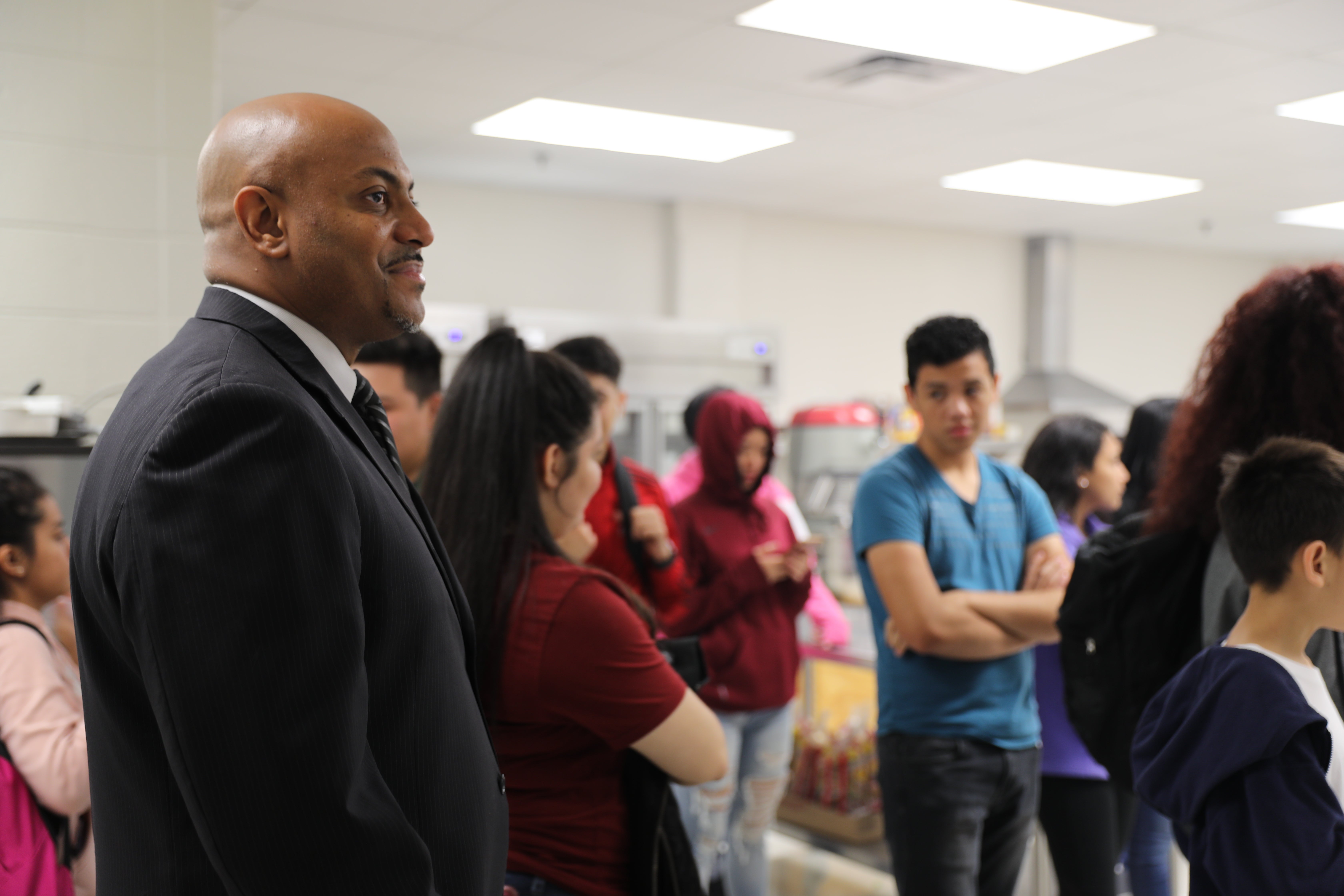 A principal stands among students in a classroom.