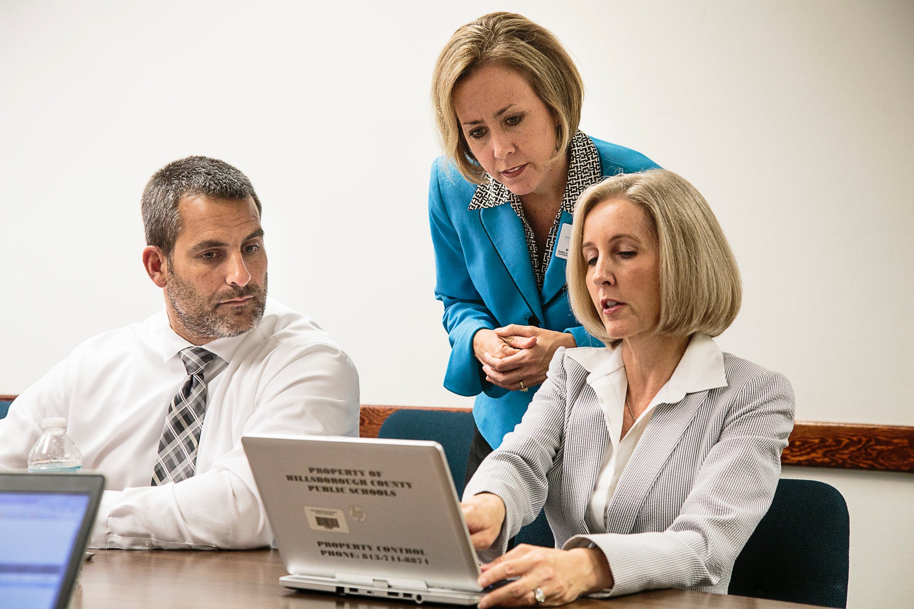 Three education leaders look at something on a laptop screen.